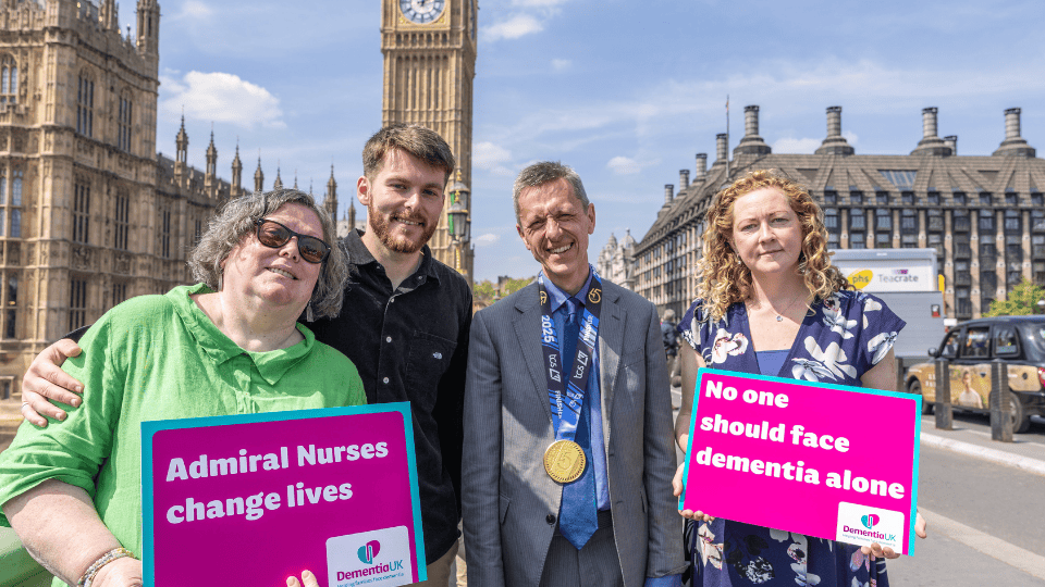 Four people stand in front of Big Ben, two holding Dementia UK signs reading “Admiral Nurses change lives” and “No one should face dementia alone.”.